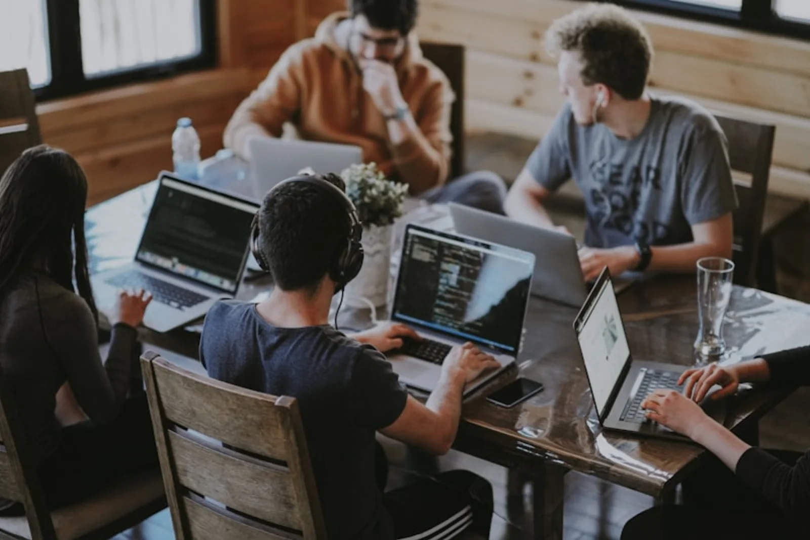 Vijf collega's rond een tafel, ieder achter een eigen laptop